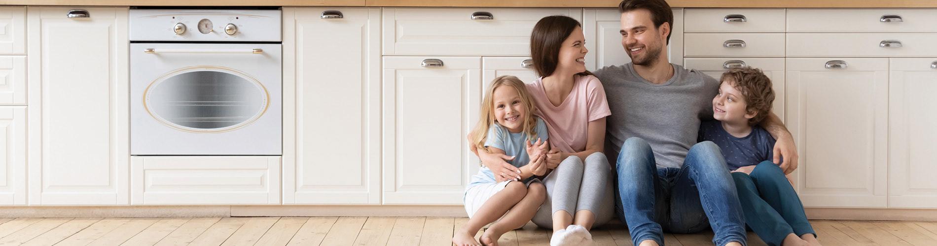 Happy family sitting on wood plank flooring in a rustic styled kitchen